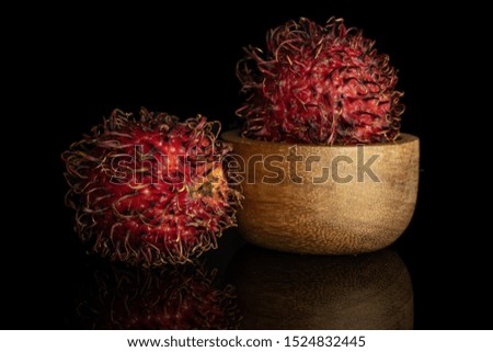 Group of two whole fresh red rambutan in wooden bowl isolated on black glass