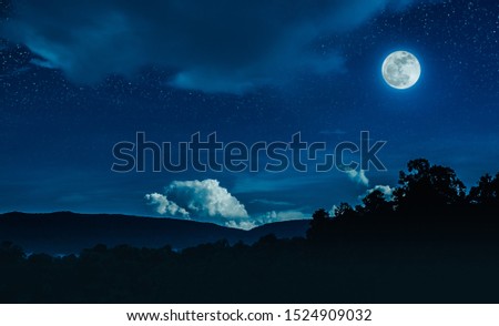 Landscape of blue night sky with many stars and cloudy above silhouette of mountain range and trees. Beautiful bright full moon over tranquil nature on dark tone.