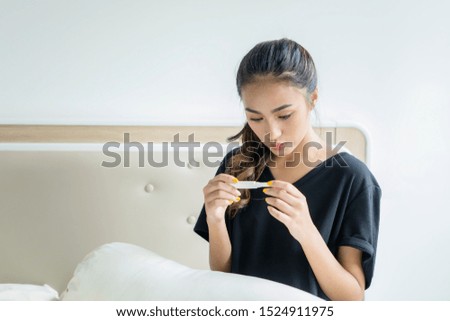 Picture of teenage girl looks worried while holding a pregnancy test and sitting in the bed