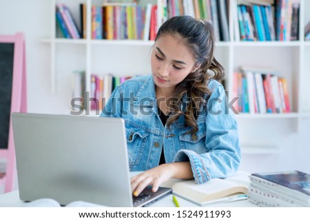Pretty teenage girl studying with computer laptop while studying in the library with bookcase background