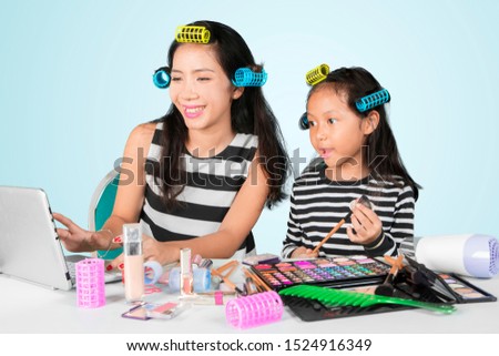 Picture of happy mother watching makeup tutorials on the laptop while doing makeup with her daughter in the studio