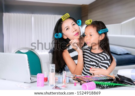 Picture of young woman doing makeup with her daughter while watching makeup tutorials in the bedroom