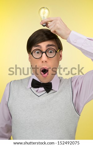 Nerd has an idea. Young nerd man holding a light bulb on his head while isolated on yellow