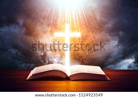 Illuminated cross on a Holy Bible. with a dramatic background sky. Royalty-Free Stock Photo #1524923549