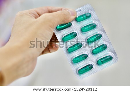 The pharmacist's hand is holding the green soft gelatine capsules in Blister packaging