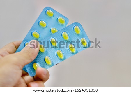 The pharmacist's hand is holding the yellow soft gelatine capsules in Blister packaging is dispensing by pharmacist.
