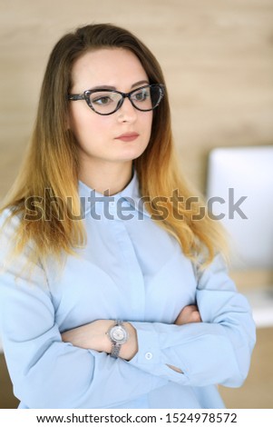 Business woman headshot at workplace in modern office. Unknown businesswoman standing straight with arms crossed. Young accountant or secretary looks good
