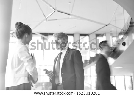 Black and white photo of mature businessman talking to secretary in office