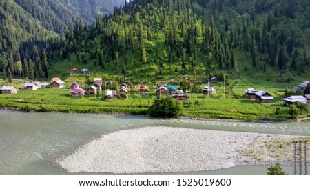 village at the base of a mountain by the river side. colorful houses surrounded by green fields