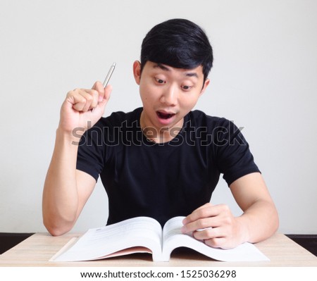 Asian man shock and excited show pen up and look at the book on the desk on white isolated
