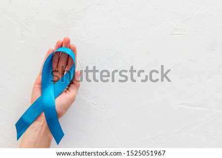 Blue ribbon in hands as symbol disease control on white background top view copy space