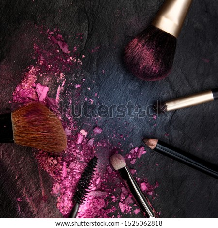 Make-up brushes with crushed cosmetics, overhead square shot on a black background forming a framewith a place for text, a beauty design template for a makeup banner