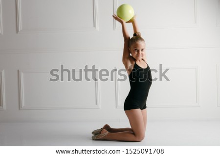 Young girl athlete rhythmic gymnastic in a black suit does exercise with the sports ball on the floor. Keeps the ball in her hands on white background