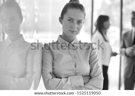 Black and white photo of businesswoman with arms crossed against colleagues in background