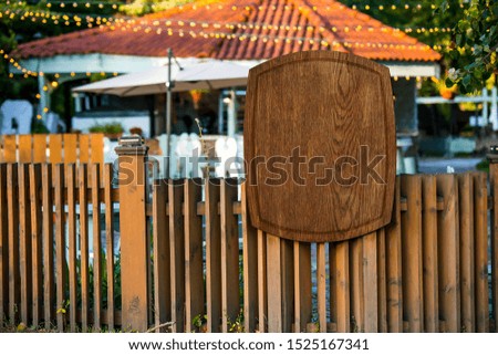 wooden brown sign close-up on a wooden fence on a blurred background of cafes and light bulbs in summer. mockup
