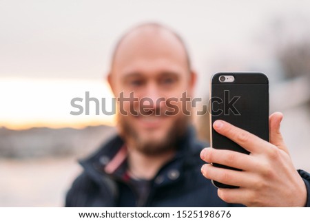 Man making photo of beautiful sea landscape on mobile phone. Happy smiling man walking outdoors, using smartphone, taking selfie, picture of sunset nature.