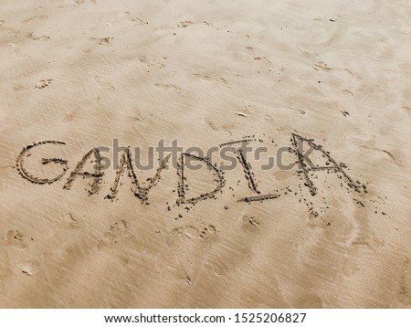 the name of the Spanish city of Gandia, the province of Valencia is written on a sandy beach in the sand