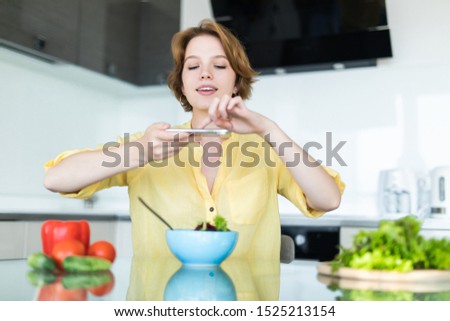 Happy woman taking a picture of salad with mobile phone while standing at the kitchen