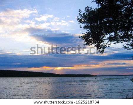Landscape photo of the forest lake at sunset - clouds illuminated by the rays of the setting sun and reflection in the water.