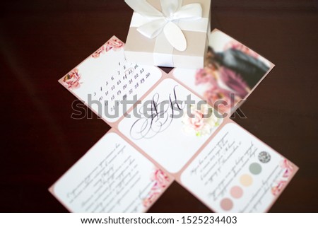 Close-up on a folding wedding invitation in the form of a paper box with a photo, text and a calendar with the image of flowers. Decor and decoration of events.