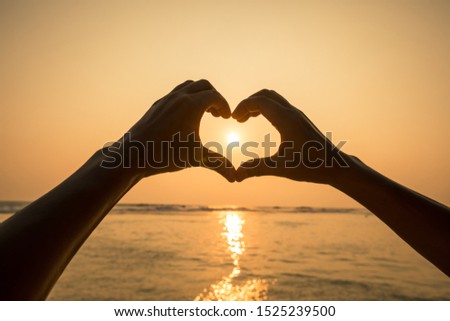 Hands in the shape of heart against the sunset over the sea.