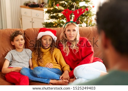 Family Sitting On Sofa Playing Game Of Charades At Christmas Together