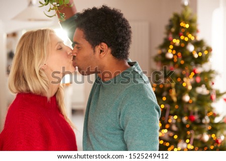 Loving Couple Kissing Under Mistletoe In House Decorated For Christmas