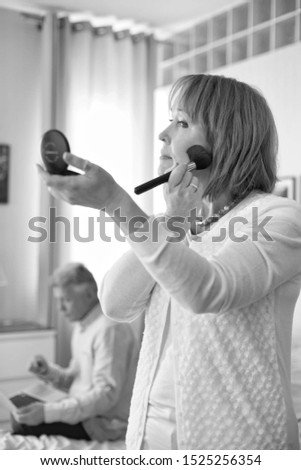 Black and white photo of Mature woman applying makeup while standing in bedroom