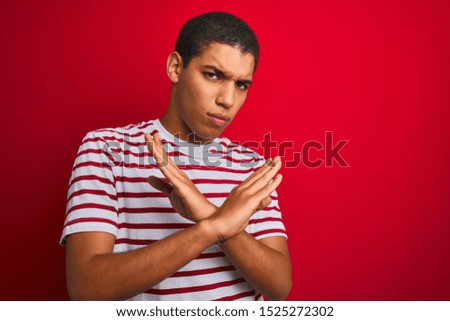 Young handsome arab man wearing striped t-shirt over isolated red background Rejection expression crossing arms doing negative sign, angry face