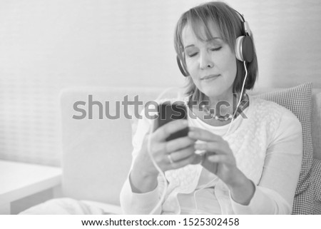 Black and white photo of senior woman listening to music in bed