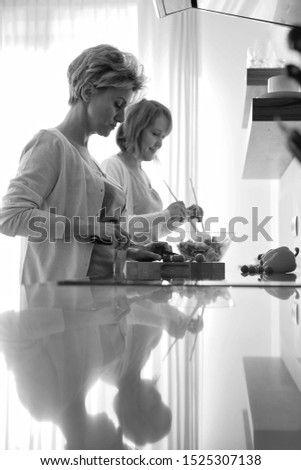 Black and white photo of Smiling mature friends preparing meal in kitchen