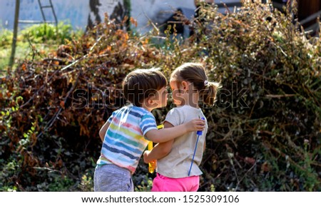 Gorgeous boy kissing his cute little sister. Portrait of sibling love. Two toddlers having fun o the grass on the beautiful sunny day. Brother and sister blowing bubbles and dancing in the park.