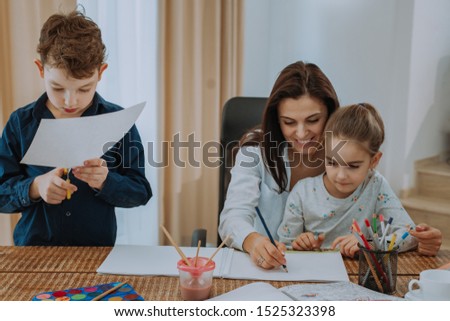 Friendly relationship between a mature mother in her two kids, they are spending a great time together while doing homework to drawing