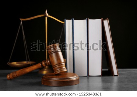 Judge's gavel, books and scales on grey table against black background. Criminal law concept