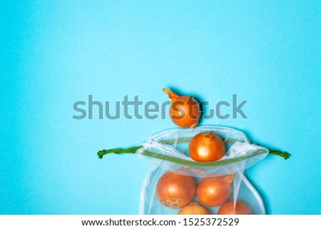 Organic golden onion in the eco bag on the trendy blue background. Place for text. Zero waste concept, plastic-free, eco-friendly shopping, vegan