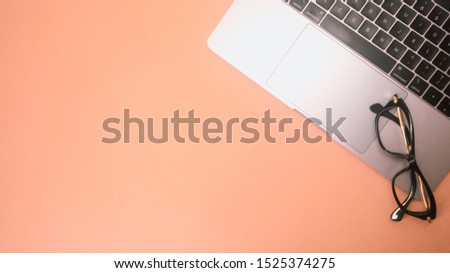 Top view of work place desk, laptop withglasses on empty bright orange background