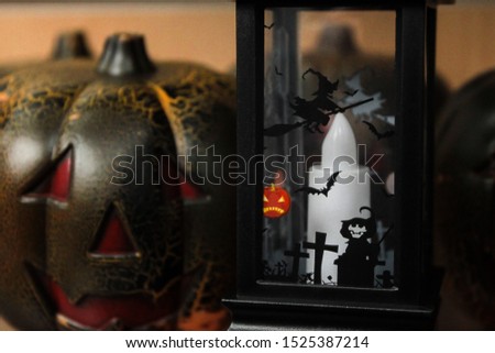 Halloween decorations: a plastic pumpkin with a brutal smile and a black lantern with a picture of a cemetery, a skeleton and a flying witch on a broomstick