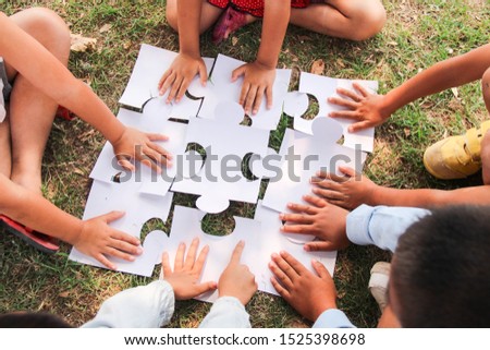 Group of ethnically diverse kids students is joined play jigsaw/puzzles pieces together in the playground. Teamwork, cooperation, learning, and education concept.