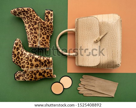 Top view on a pair of trendy leopard print boots, crocodile crossbody bag, leather gloves, and makeup products. Flat lay of feminine trendy accessories in green and beige tones.