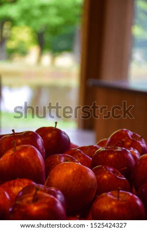 close up of red delicious apples piled up in orchard store with pond and trees in bokeh background wooden archway