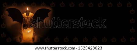 Halloween background. The human skeleton sits near a candle. Place for text. In the frame of pumpkins.