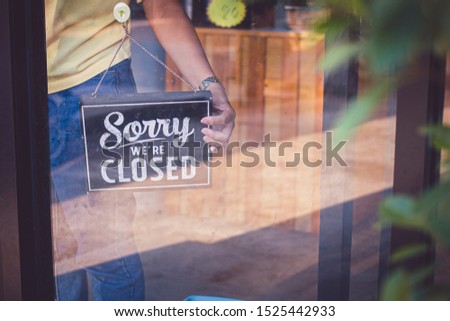 Woman Holding up a shop sign saying: Sorry we're Closed