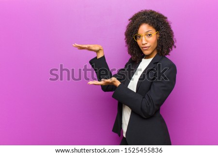 young black business woman holding an object with both hands on side copy space, showing, offering or advertising an object