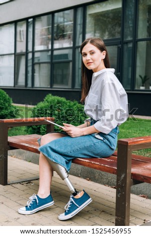 attractive disabled woman sitting on bench with digital tablet