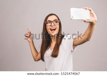 Portrait of a smiling cute young woman making selfie photo on smartphone isolated against grey background.