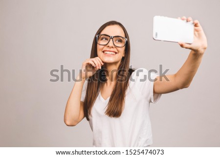 Portrait of a smiling young cute woman making selfie photo on smartphone isolated against grey background.