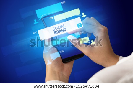 Female hand typing on smartphone with SOCIAL BRAND inscription, social networking concept