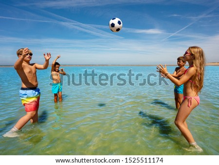 Group of happy cute kids play volleyball in water