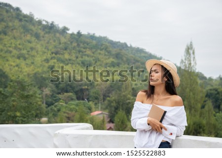 closeup asia woman in white shirt hand hold the book to read at the edge of balcony with sunlight over the hill