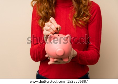 Redhead woman with turtleneck sweater holding a big piggybank